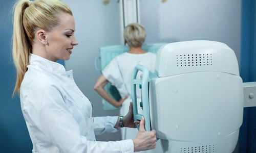 A smiling nurse preparing a patient for a preventative screening or mammogram exam in her 40s