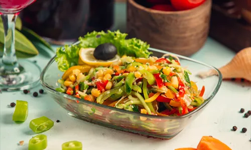 Colorful vegetable salad with corn, bell peppers, cucumber, and fresh greens in a glass bowl