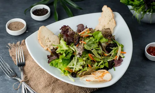 Mixed green salad with leafy vegetables, shredded carrots, dried fruit, and toasted bread slices