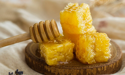 Golden honeycomb cubes with a honey dipper on a wooden tray.
