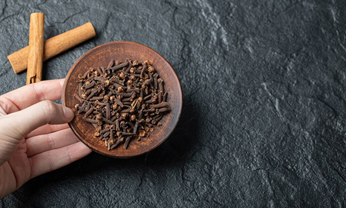 A wooden bowl of dried cloves with cinnamon sticks.