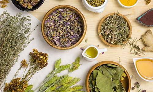 Natural spa items with dried flowers, bath salts, soap bar, and honey dipper on a gray surface.