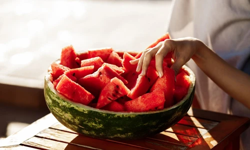 A hand picking up a fresh slice of watermelon