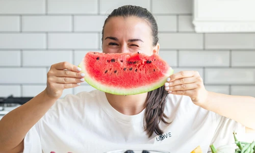 Woman holding a watermelon slice shaped like a smile and other foods on the table