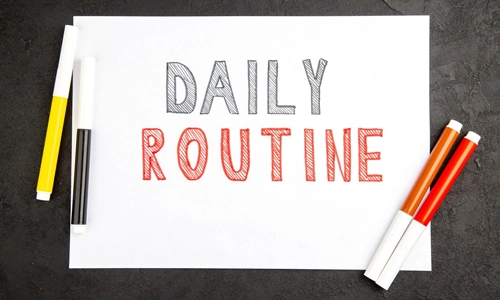 Top view of written daily routine on white paper with markers on dark surface