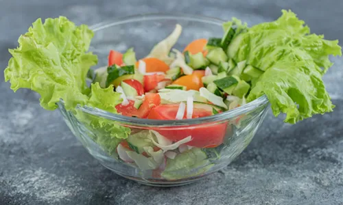 Top view Pomegranate salad served on fresh lettuce leaves on a white plate with notepad on light background