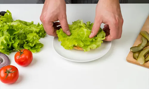 Hands preparing a fresh burger topped with lettuce and vegetables
