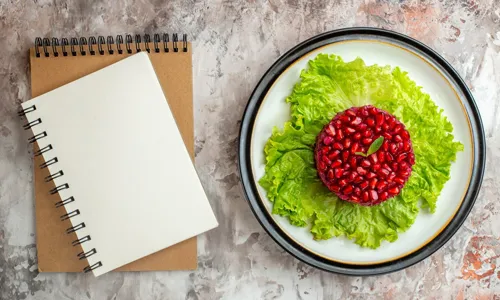 Top view delicious pomegranate salad round shaped on green salad with notepad on light background