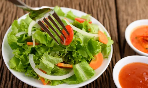 Fresh green salad with lettuce, onions, carrots, and tomatoes served with dressing.