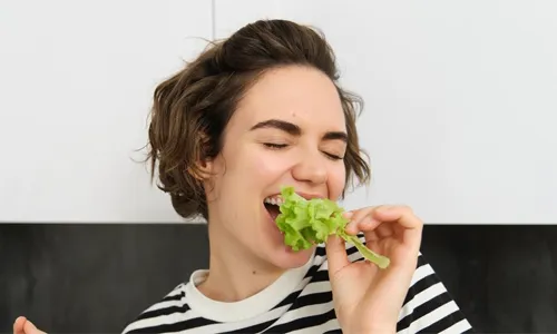 Close up of funny cute woman vegetarian eating lettuce leaf and smiling concept of healthy diet girl