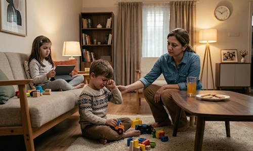 Mother comforting a crying young boy while his sister uses a tablet in the living room