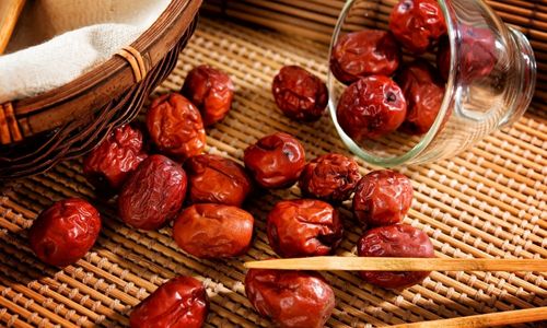 Dried chinese jujube fruit scattered on a woven mat beside a glass jar and wooden chopsticks.