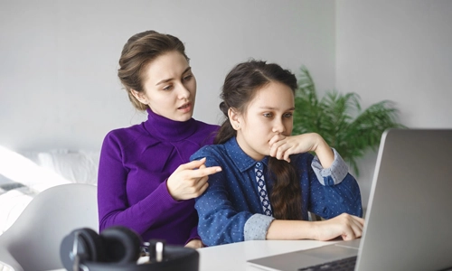 Mother helping her teenage daughter with schoolwork on a laptop