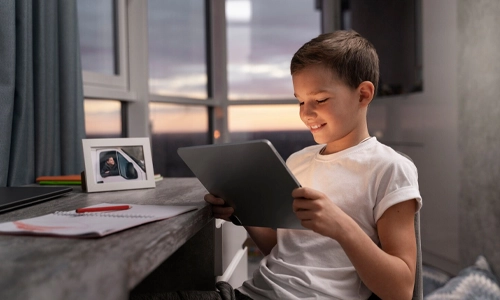 Child sitting on a bed while using a tablet device