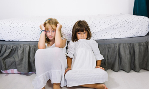 two young children sitting on the floor in front of a bed.