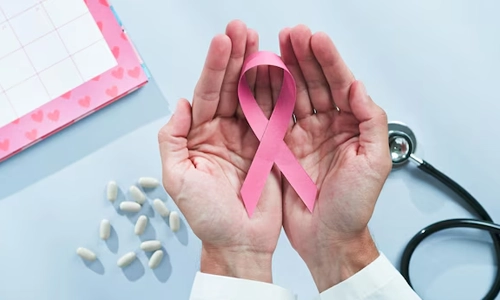 A doctors hands holding a pink ribbon in a background of pills, report and stethoscope