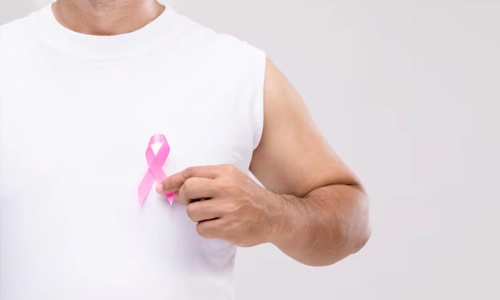 Man pointing to a pink breast cancer awareness ribbon on his shirt, promoting breast cancer education and support