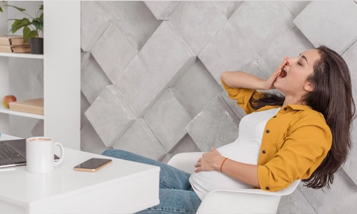 Image of a pregnant women yawning in front of a laptop and smartphone.