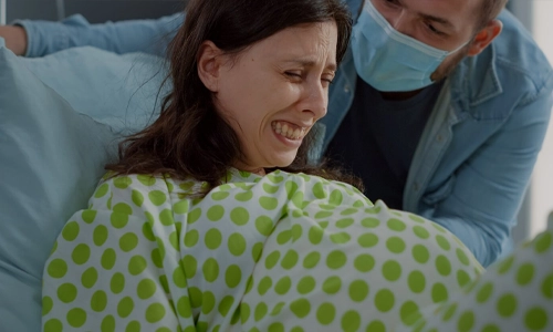 Pregnant woman in active labor in a hospital bed with her husband providing assistance and comfort.