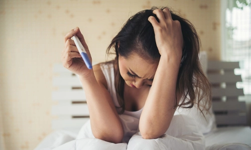 Woman sitting on a bed looking at a negative pregnancy test, representing the emotional start of the journey toward assisted reproduction.