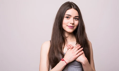 Smiling woman with hands on her chest, illustrating breast tenderness as a common early sign of pregnancy.