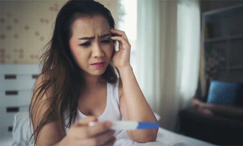 Sad woman holding a pregnancy test sitting on her bed, illustrating the emotional impact of false pregnancy.