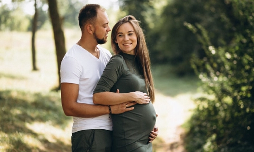 Husband walking with his pregnant wife in a park, representing the crucial role of paternal support for healthy pregnancy outcomes.