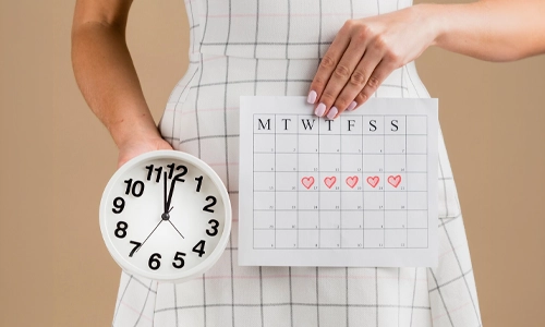 Close up of a hand marking a period calendar to track ovulation and fertile windows.