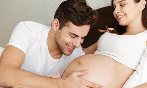 Happy pregnant wife lying in bed with her husband, illustrating emotional validation and partner bonding during the third trimester.