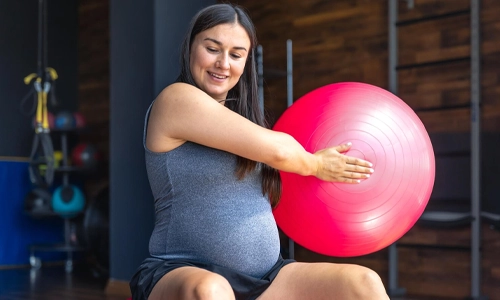 Image of a pregnant women doing light exercise with fit ball in gym