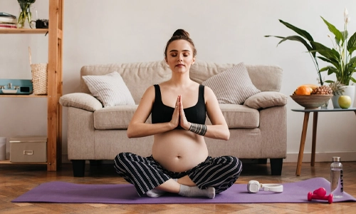 Image of a pregnant woman meditating and doing yoga in the living room.