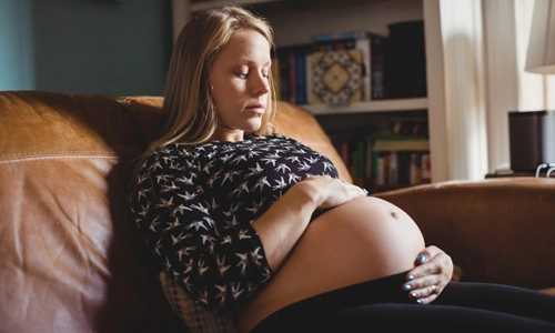 A pregnant woman relaxes in a cozy sofa in a living room, with her hand on her belly