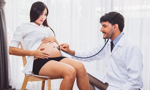 Healthcare professional checking a pregnant woman with a stethoscope during a routine hospital visit.