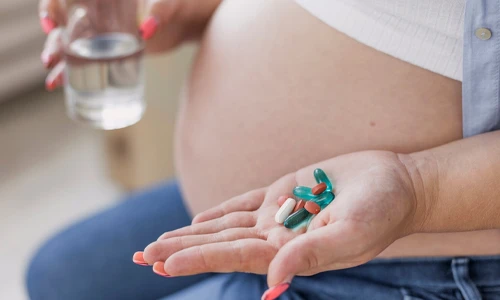 Pregnant woman holding prenatal vitamin pills to prevent nutrient deficiencies.