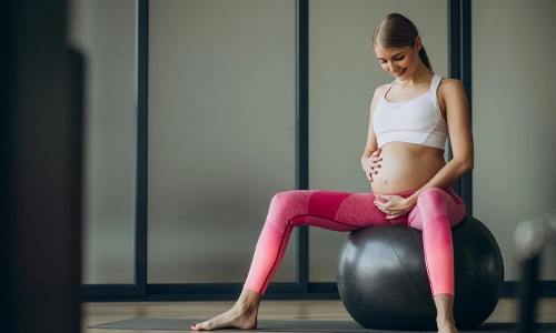 Pregnant woman exercising with a fit ball in a pilates class for strength and stability.
