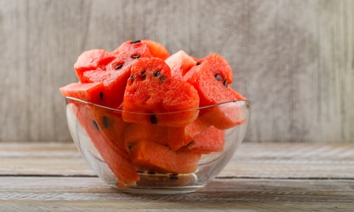 Ripe watermelon pieces in a glass bowl on wooden and grunge background. Side view.